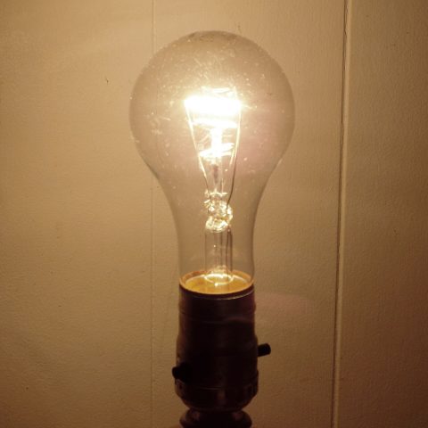 A glowing incandescent light bulb with visible filament