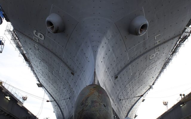 Shipyard workers beneath the hull of the USS Bonhomme Richard in a dry dock