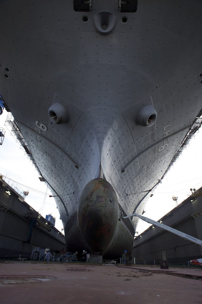 Shipyard workers beneath the hull of the USS Bonhomme Richard in a dry dock